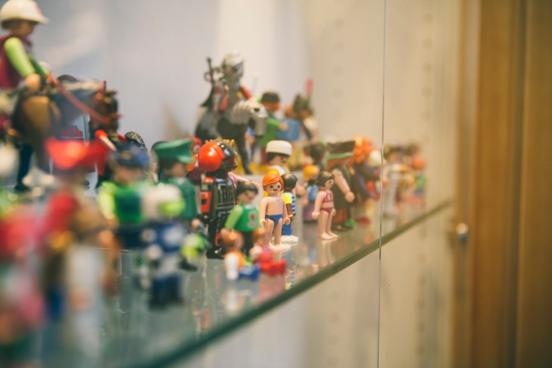 Display case containing numerous colorful Playmobil figurines and accessories arranged on a glass shelf.