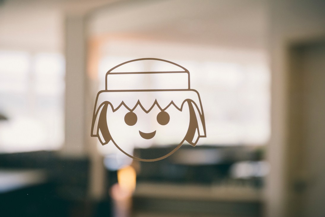 Playmobil character logo with smiling face and feathered headdress printed on glass.
