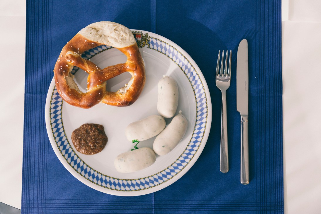 Bavarian Weisswurst meal with pretzel, sausages, mustard, and soft cheese on traditional blue and white patterned plate.