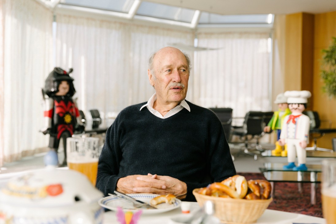 Horst Brandstätter seated at a conference table with Playmobil figurines and pretzels visible.