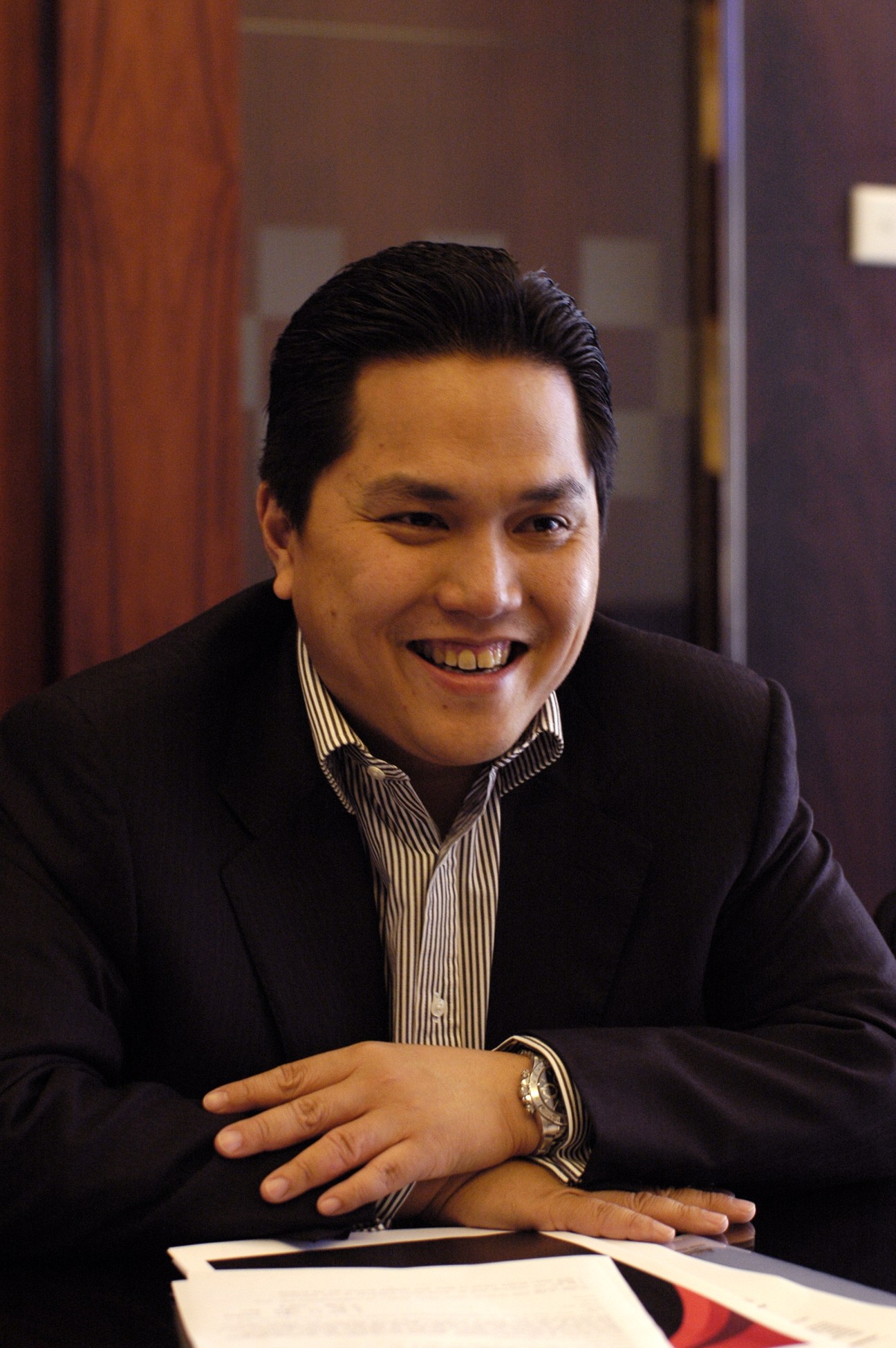 Erick Thohir, founder of Mahaka Media group, smiling at a desk in business attire.