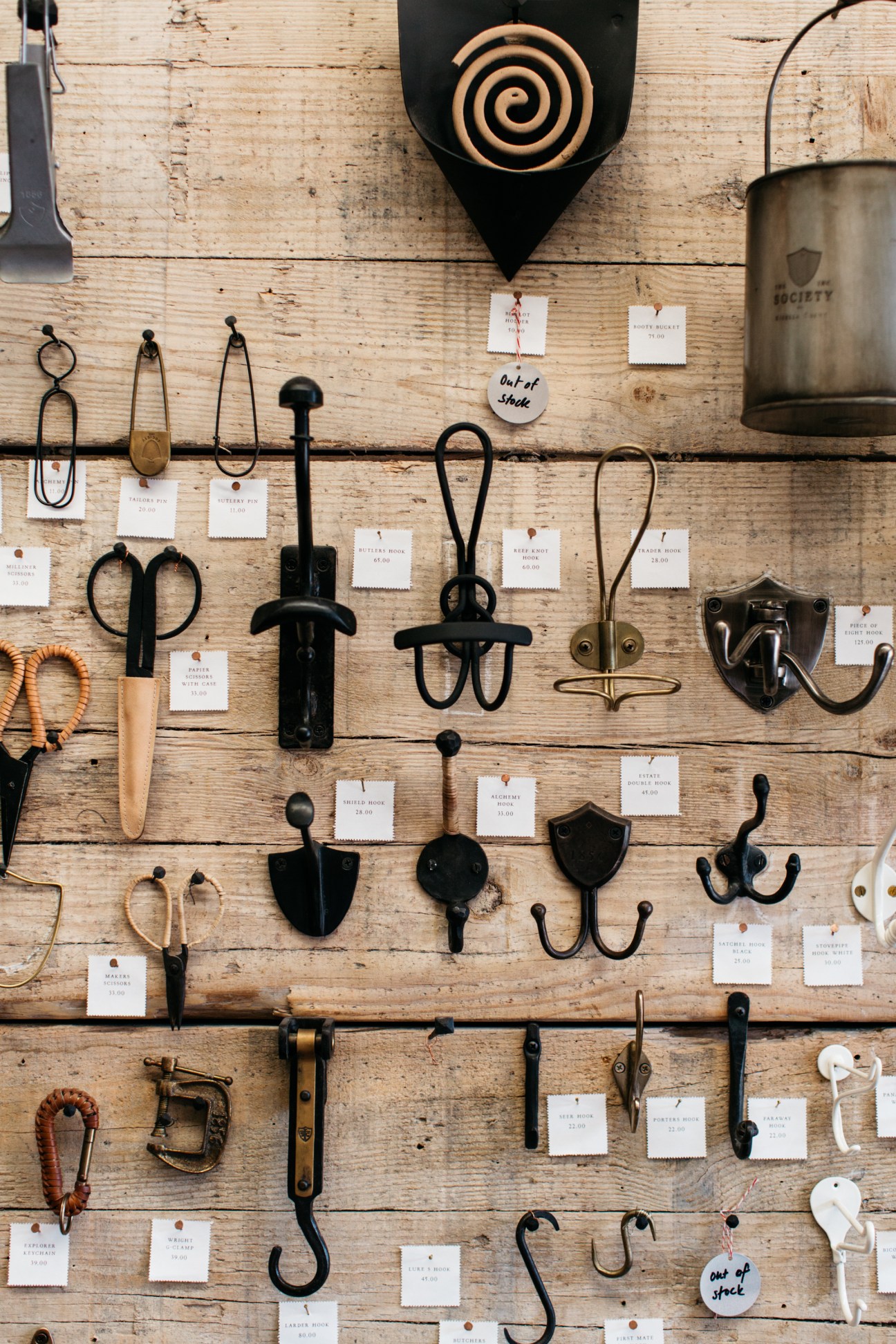 Wall display of various metal hooks, handles, and hardware items with price tags at The Society Inc.