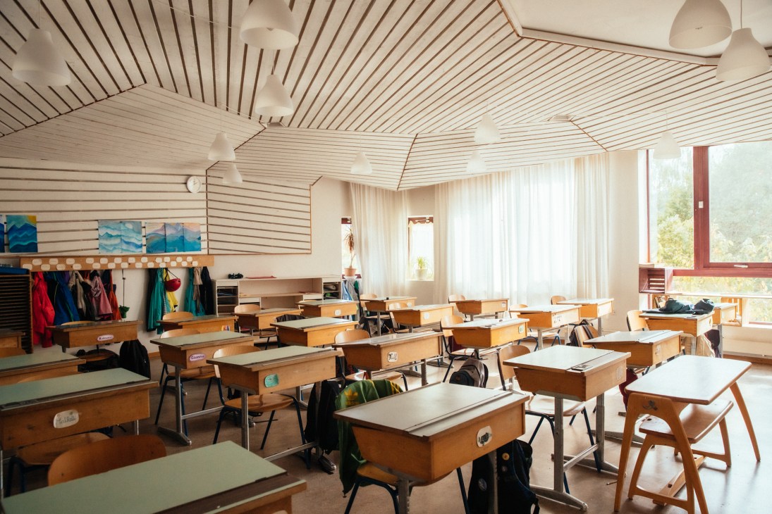 A bright classroom with wooden desks, chairs, striped ceiling, and large windows at a Geneva school.