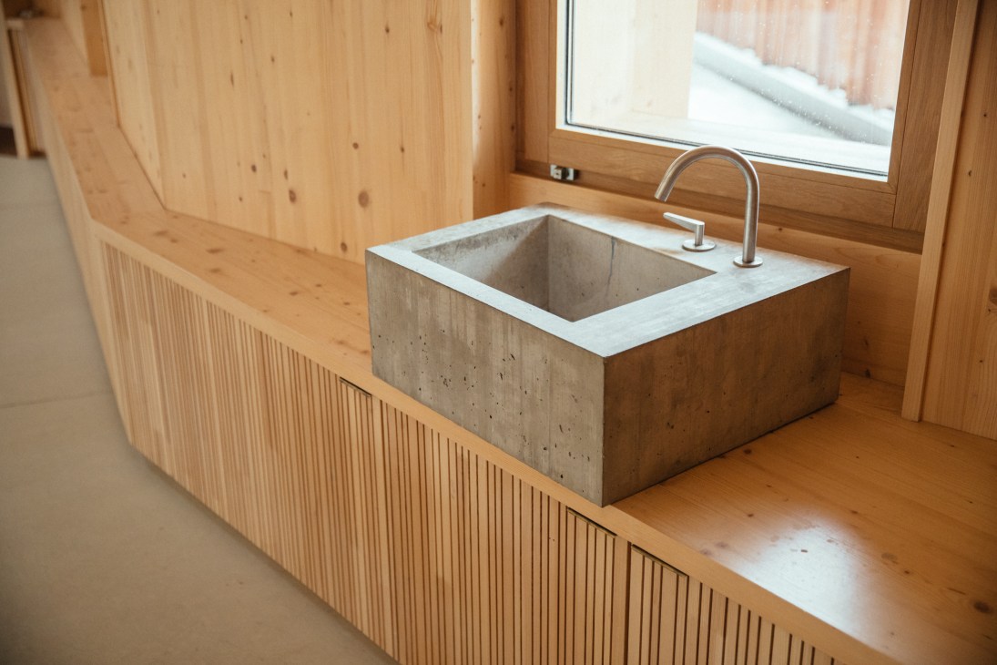 A concrete sink with white surround in a wooden-lined classroom with a modern faucet and large window.