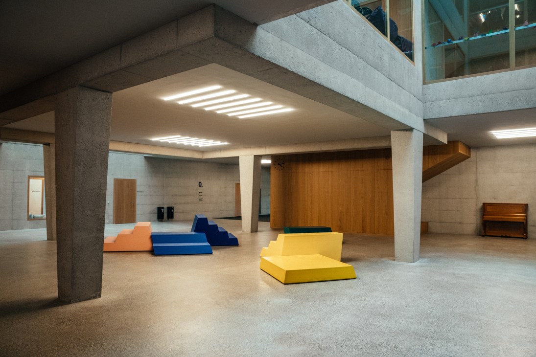 Colourful foam sculptures in blue, yellow and orange sit in a concrete and oak school entrance hall with skylights.