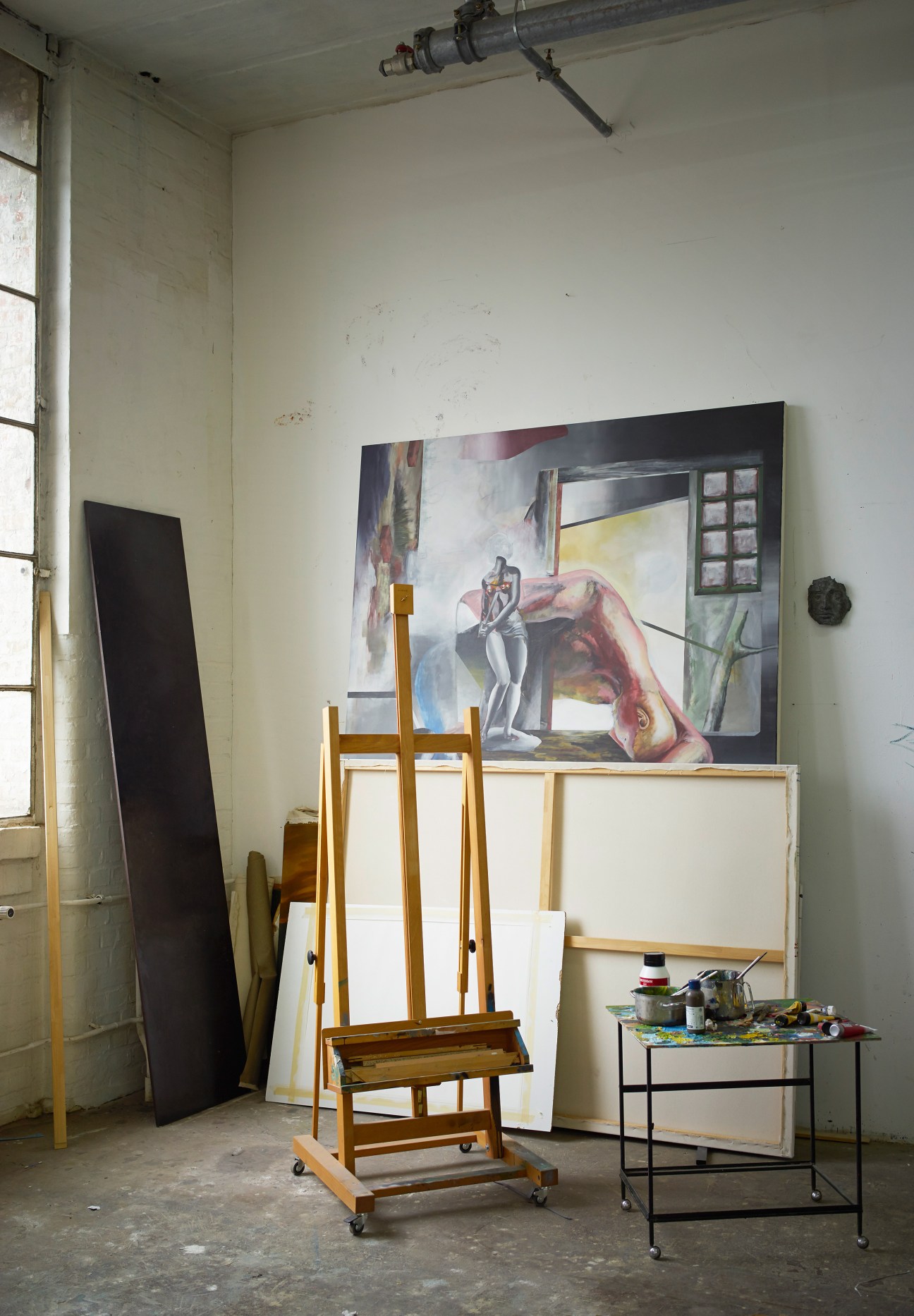 Artist's studio with easel, painting in progress, and art supplies in an industrial space.