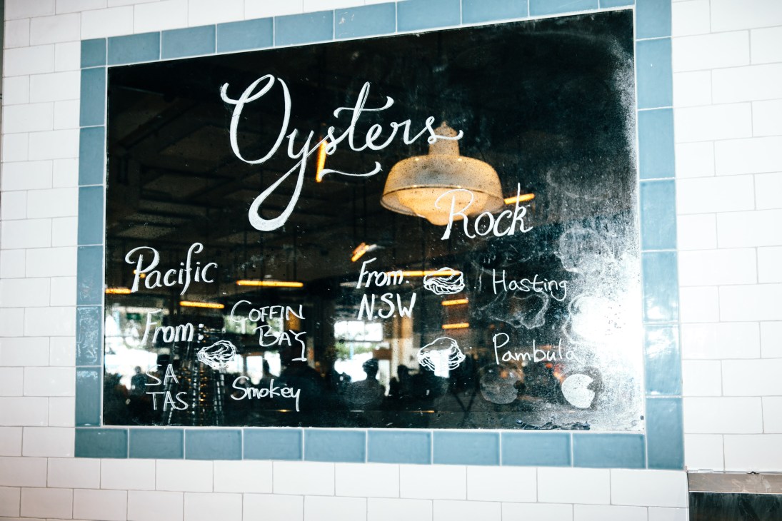 Hand-written oyster menu on black board listing Sydney Rock and Pacific oysters from various Australian regions.