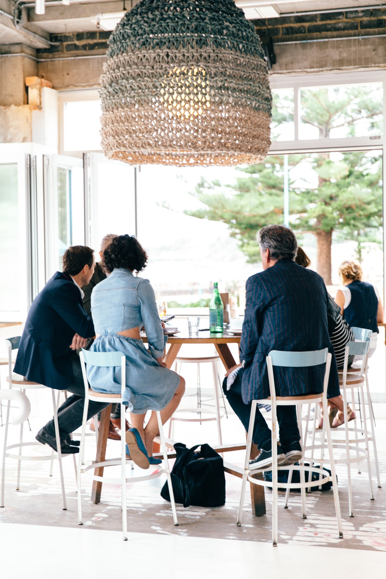 Four people seated at a table under a woven pendant light during a lunch discussion at Coogee Pavilion in Sydney.