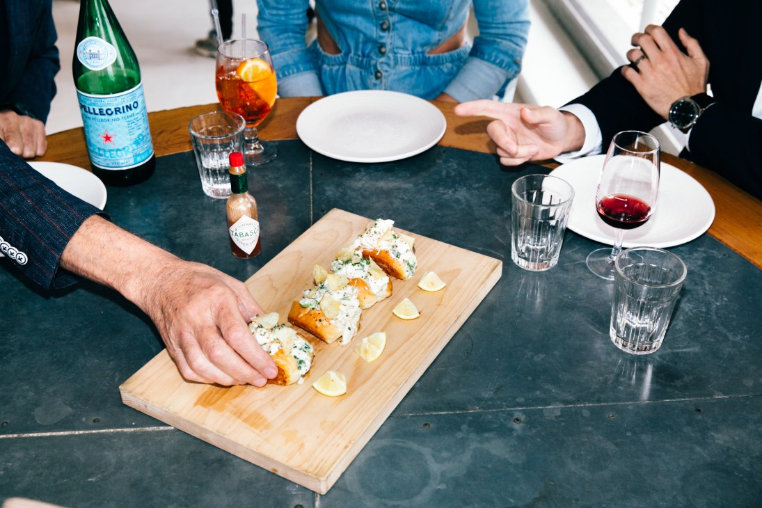 Mini lobster rolls with celery, lemon mayo and chives served on a wooden board at a dining table.