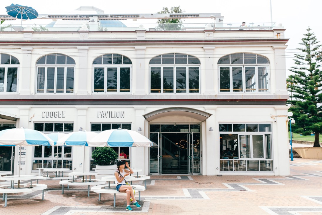 White beachside building with blue and white umbrellas and outdoor seating at Coogee Pavilion.