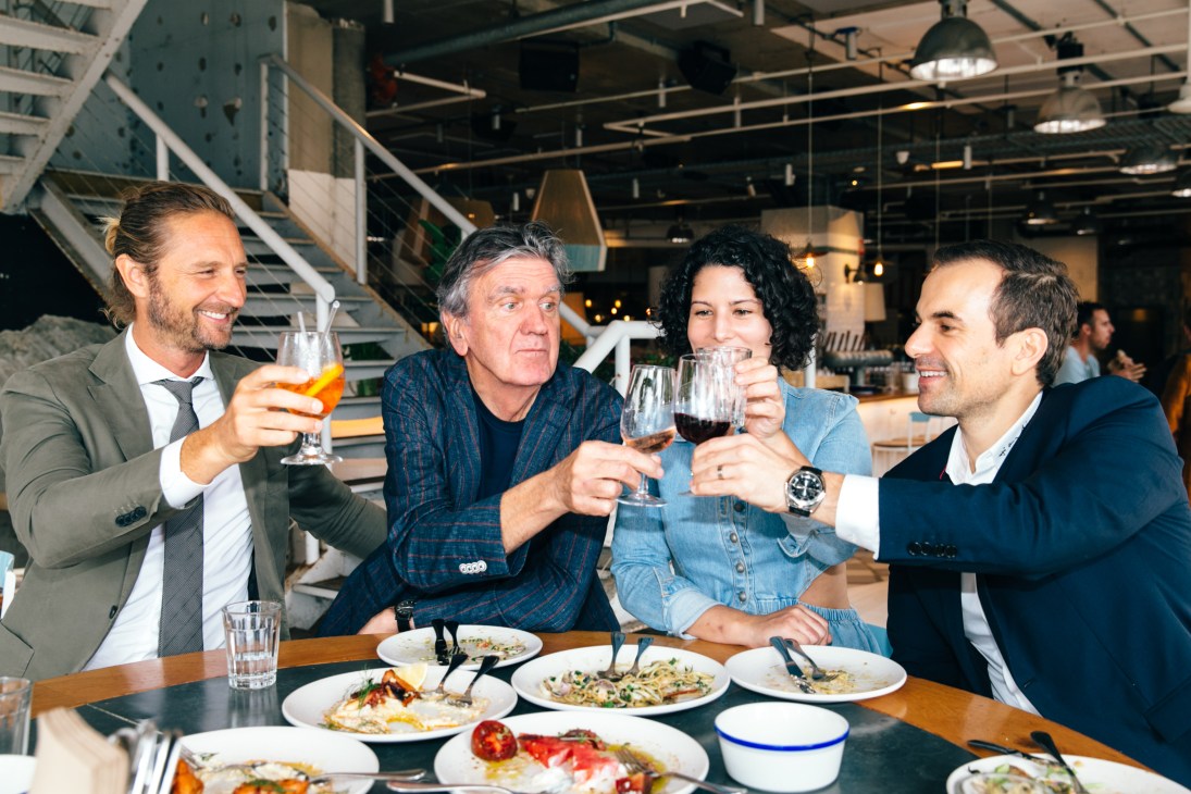 Justin Hemmes, Terry Durack, Analiese Gregory and Peter Andrews clink glasses at a dining table.