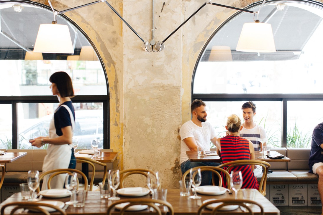 Interior of The Apollo restaurant with Artemide lamps, Thonet chairs, and diners by large windows.