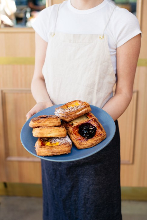 Person in white apron holding blue plate with pastries at Garçon bakery.