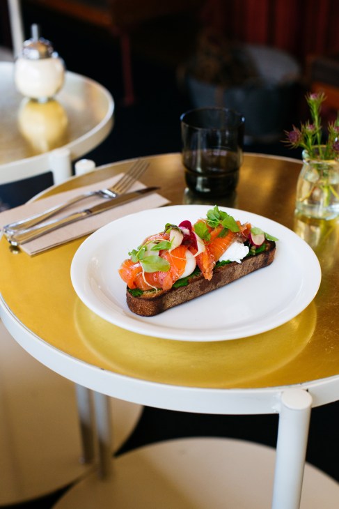 Plated open-faced smoked salmon sandwich with white cream cheese, microgreens and beets on dark bread at Butcher and the Farmer.