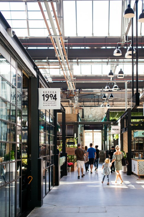 Interior of Bodega 1904 restaurant and wine shop at Tramsheds with industrial ceiling, pendant lights, and customers walking through.