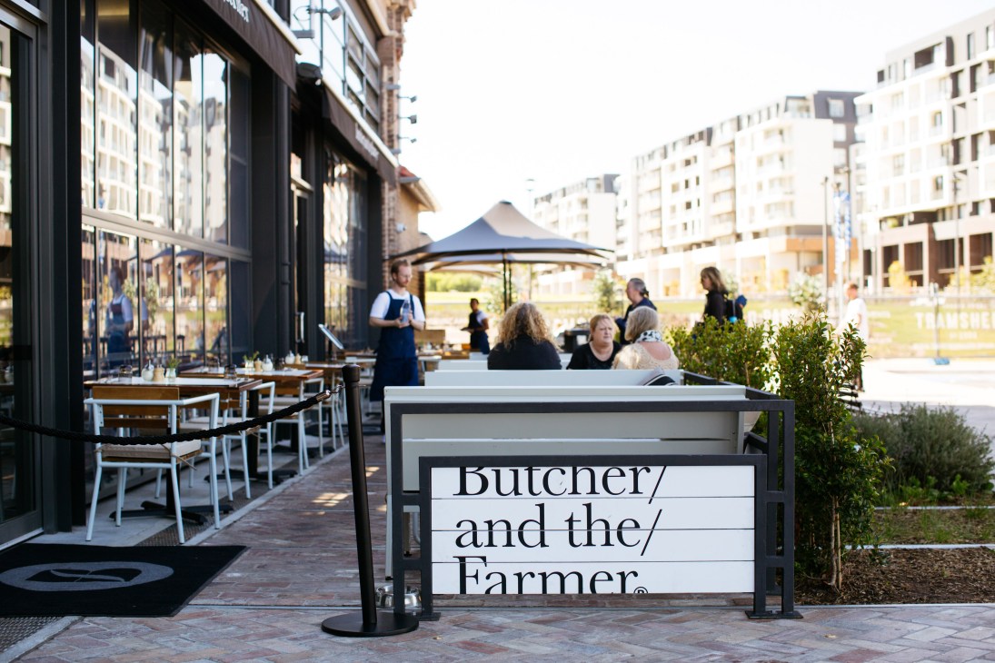 Outdoor dining area at Butcher and the Farmer restaurant with customers seated under a black umbrella.