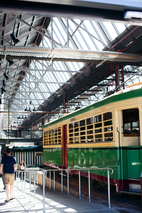 Vintage green and cream tram carriage displayed inside Tramsheds market hall with industrial ceiling.