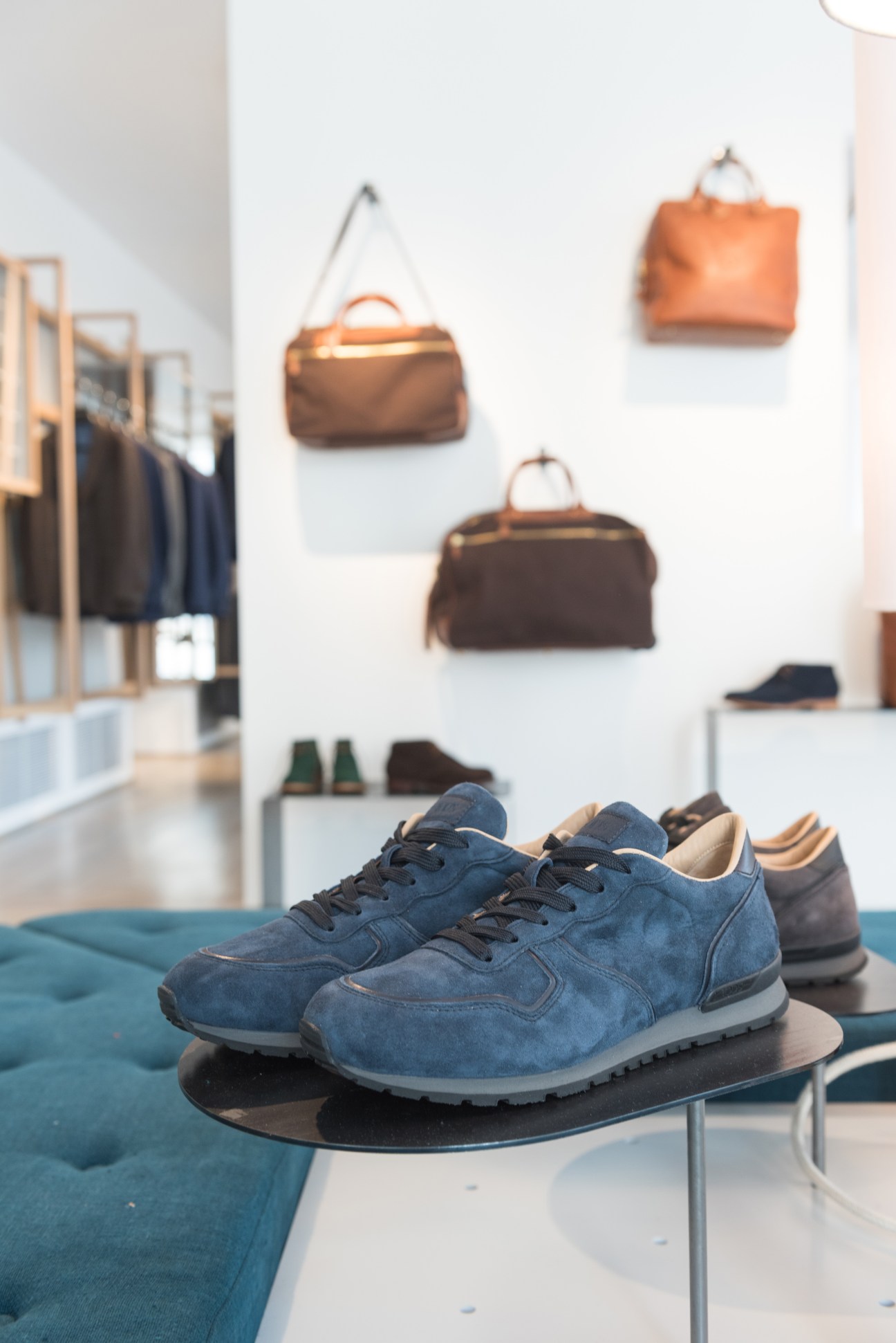 Blue suede sneakers displayed in Dantendorfer shop with handbags and clothing visible in background.