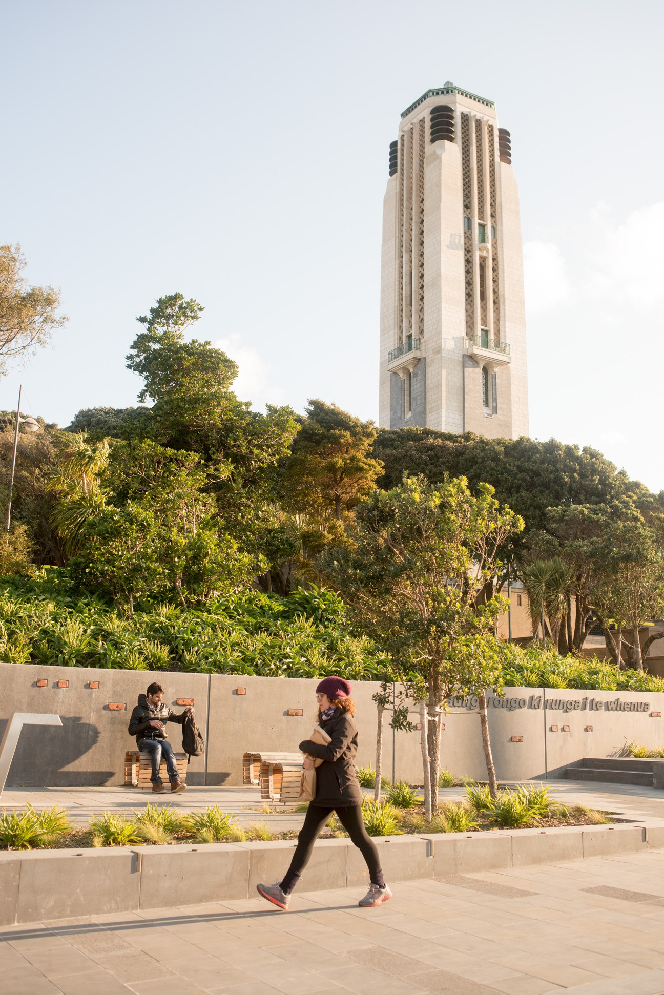 A tall Art Deco carillon tower overlooking a terraced memorial plaza with trees and people.
