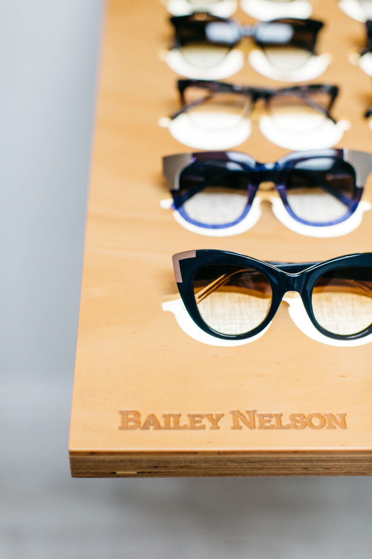 Bailey Nelson eyeglasses displayed on a wooden board showing various frame styles and colors.