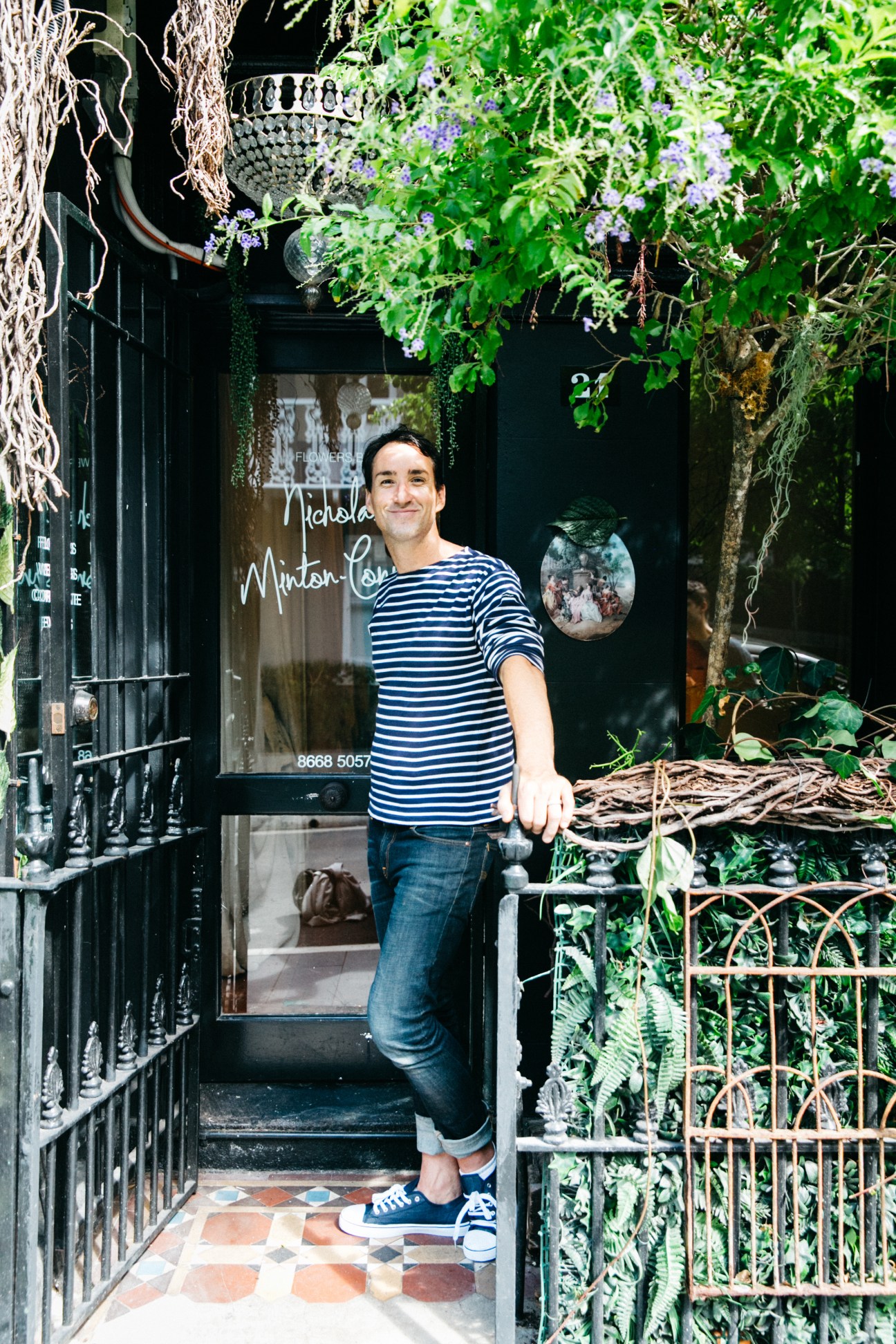 Nicholas Minton Connell stands outside Pollon Flowers storefront surrounded by hanging plants and flowers.