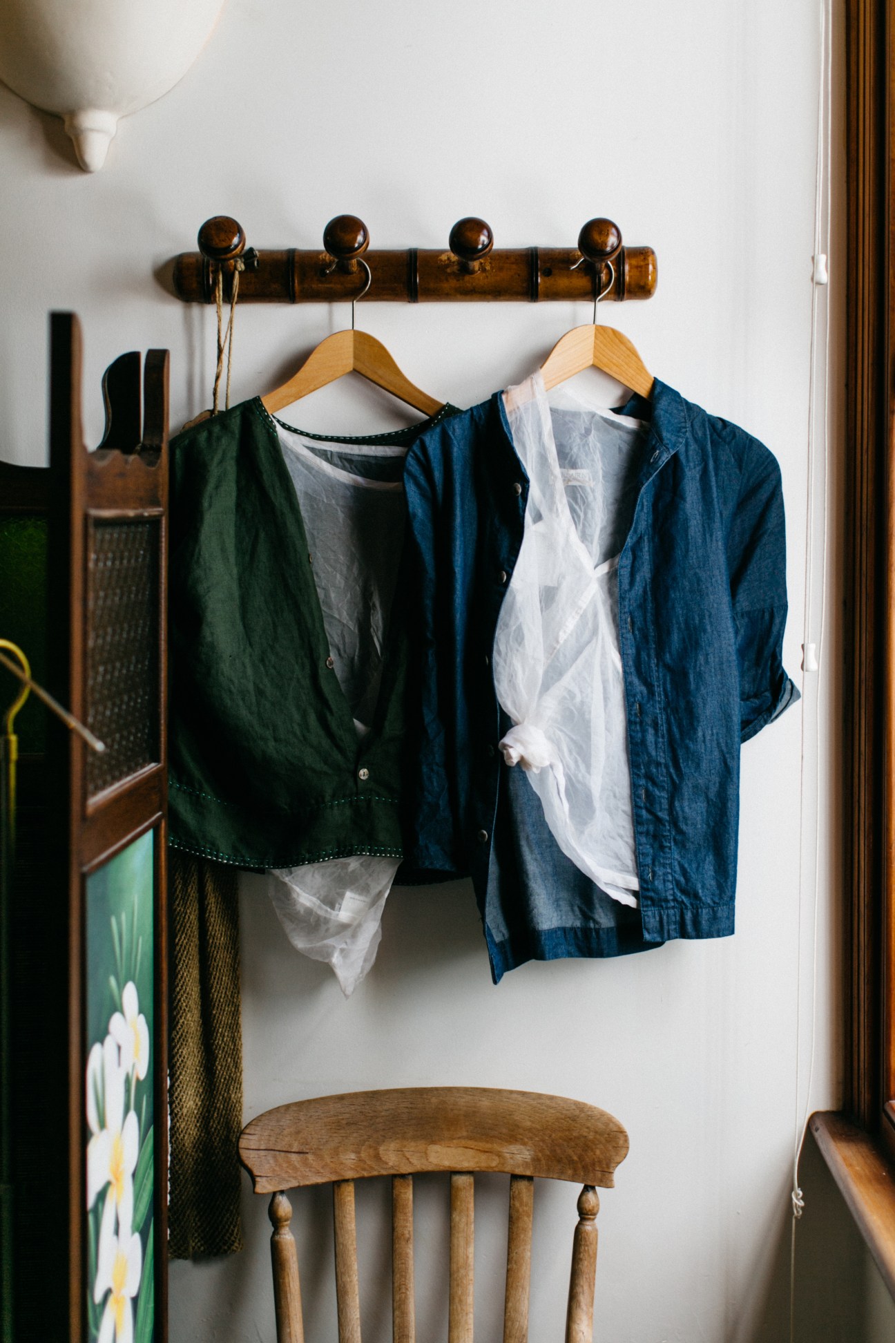 Clothing displayed on wooden hangers from a dark wooden rail with brass finials.