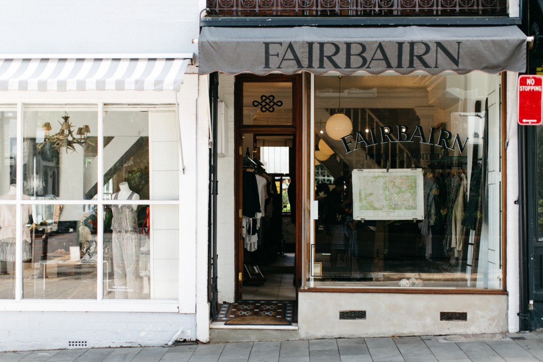 Fairbairn storefront on William Street with grey awning, wooden door, and window display of clothing.