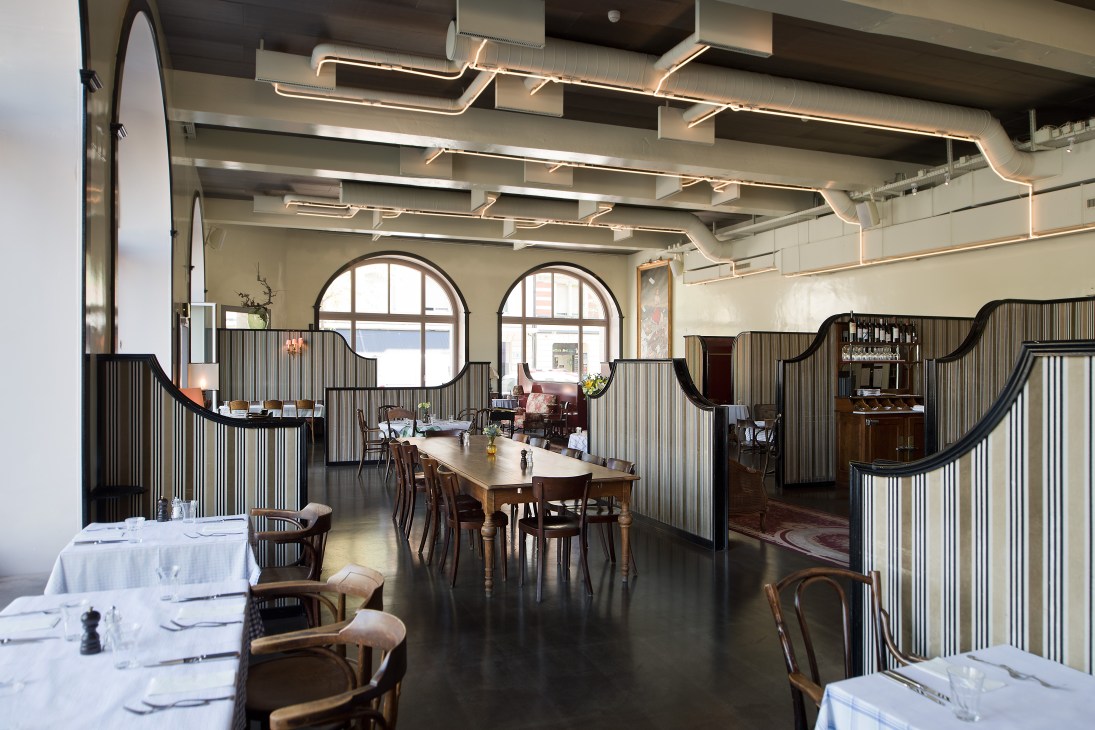 Modern restaurant interior with wavy metal partitions, wooden tables, and arched windows at Volkshaus.