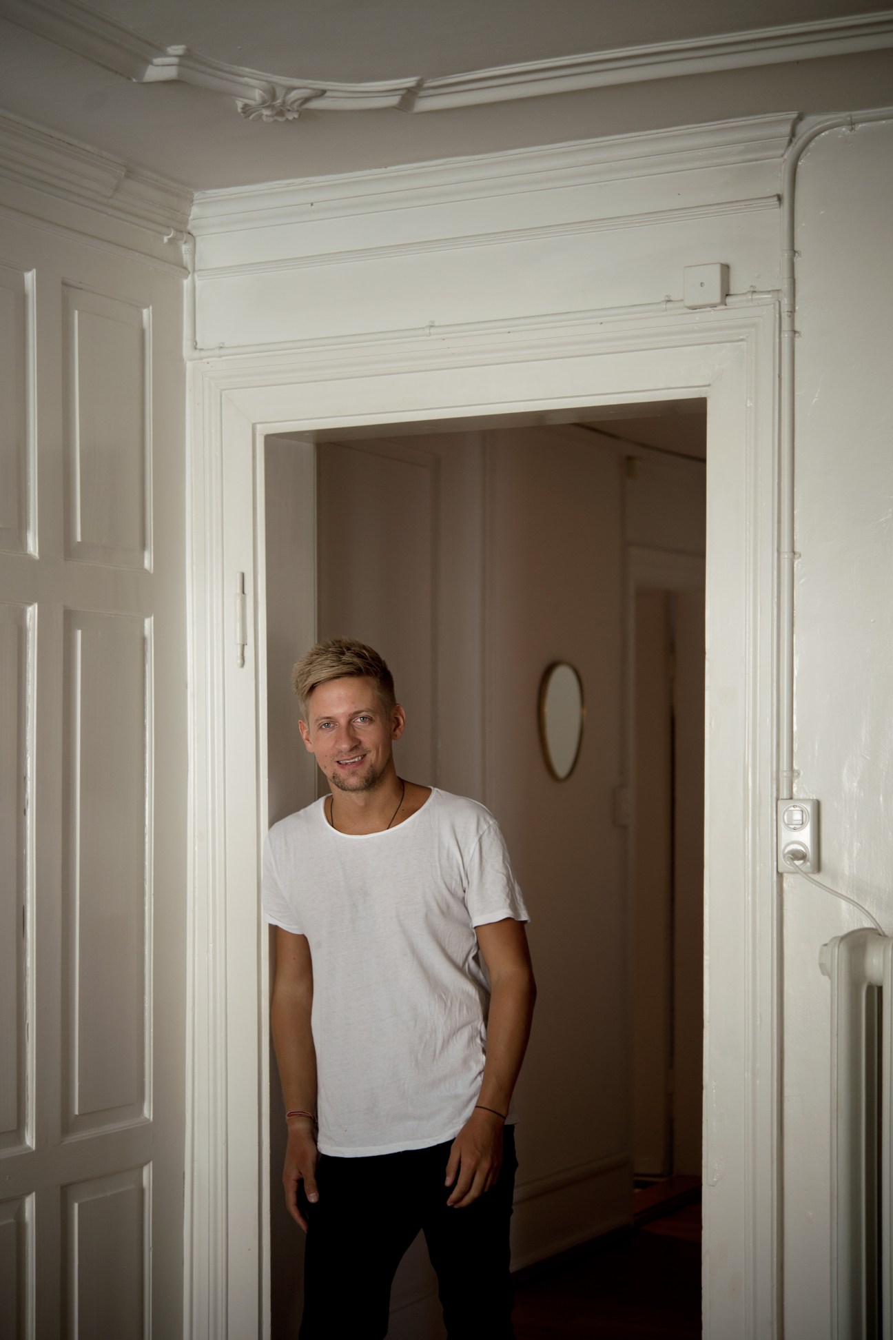 Florian Fleischmann, a yoga teacher and designer, stands in a doorway wearing a white t-shirt.
