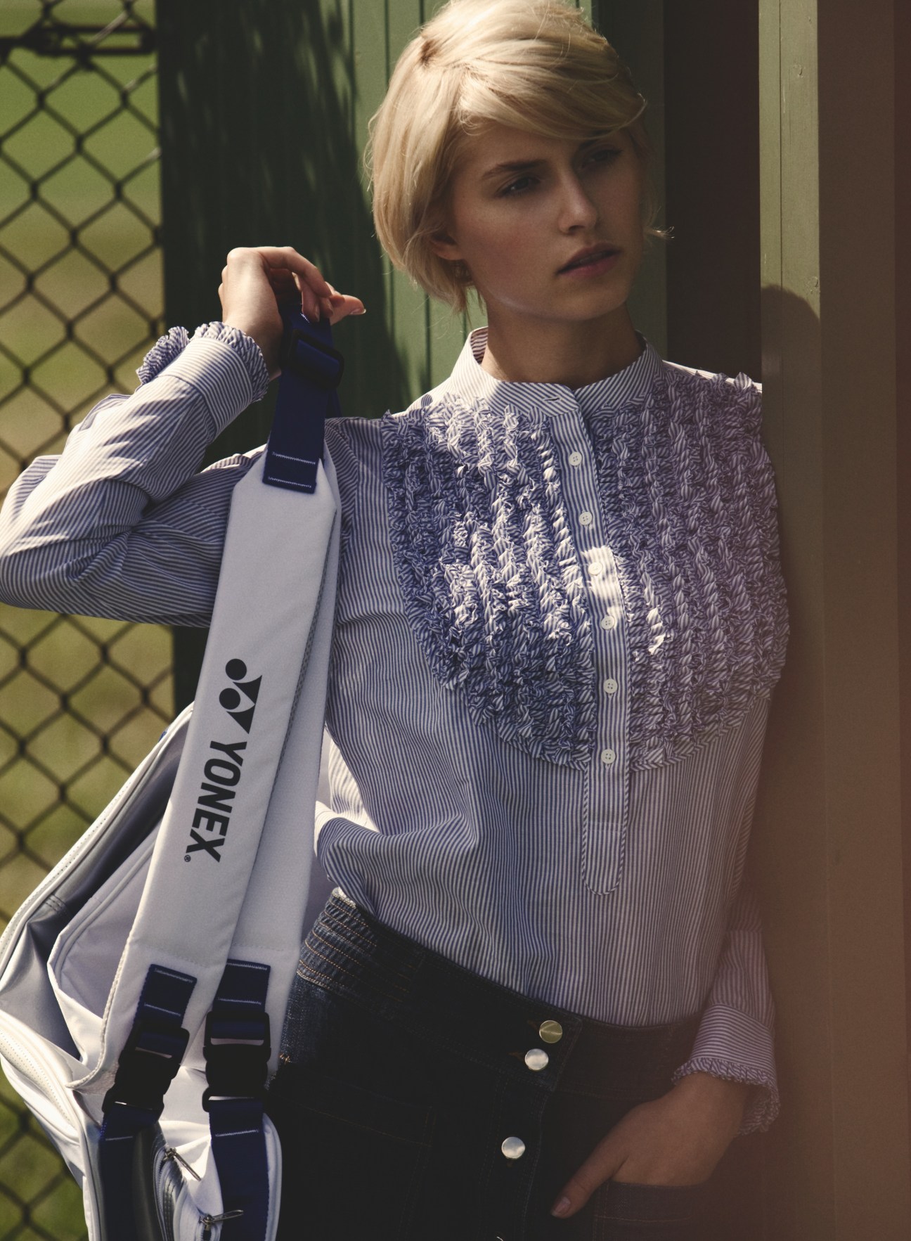 Model holding Yonex racquet bag wearing Drawer shirt and Madras skirt at tennis court.