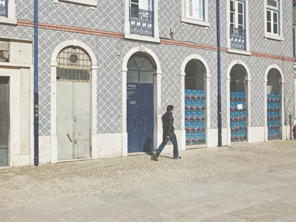 Person walking past a historic Portuguese building with blue-and-white azulejo tiles and arched windows.
