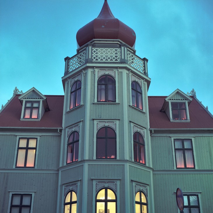 Icelandic building with distinctive architecture featuring a burgundy onion dome, pale green walls, and large arched windows illuminated at dusk.