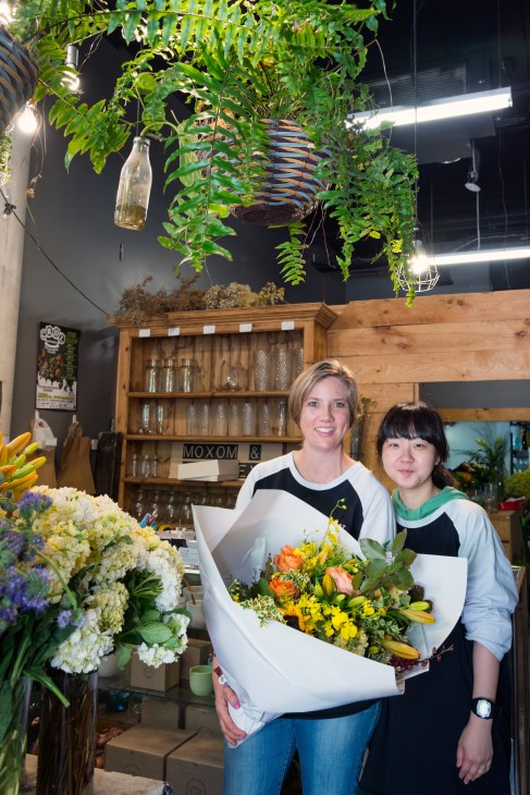 Two female staff members holding a colorful flower bouquet inside Moxom and Whitney florist in Braddon.