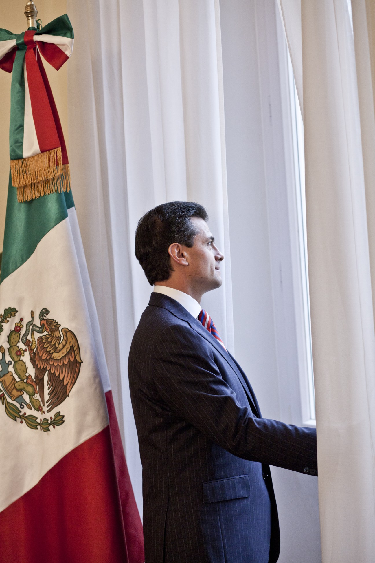 Enrique Peña Nieto in profile wearing a dark suit beside the Mexican flag.