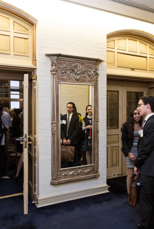 Undergraduate students in formal attire mingle at a dinner event in Riggs Library, an ornate historic space with white walls and decorative architectural details.
