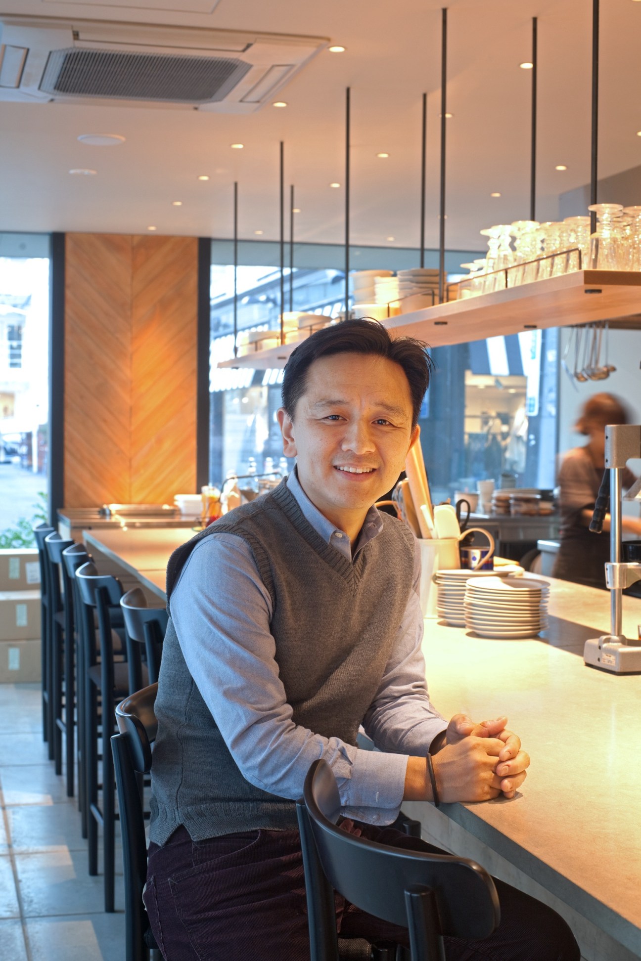 Masaki Yokokawa of Welcome stands at a counter in the Three Aoyama restaurant, smiling at the camera.