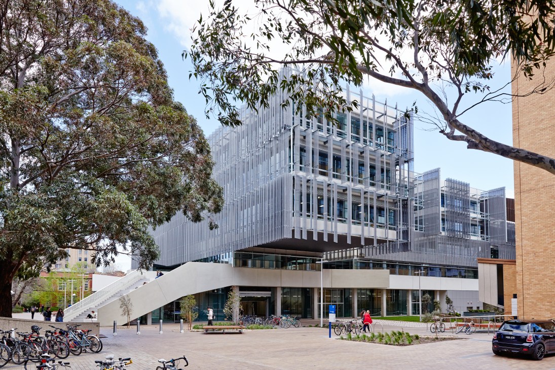 Melbourne School of Design exterior showing perforated zinc facade, wide staircase, and plaza with bicycles and people.