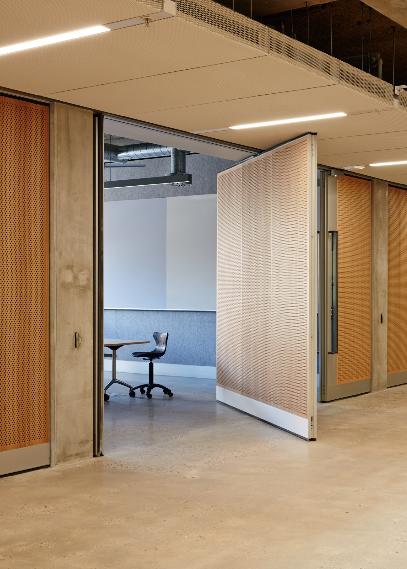 Revolving wooden and glass doors open a studio workspace with chair and blue acoustic panel visible inside.