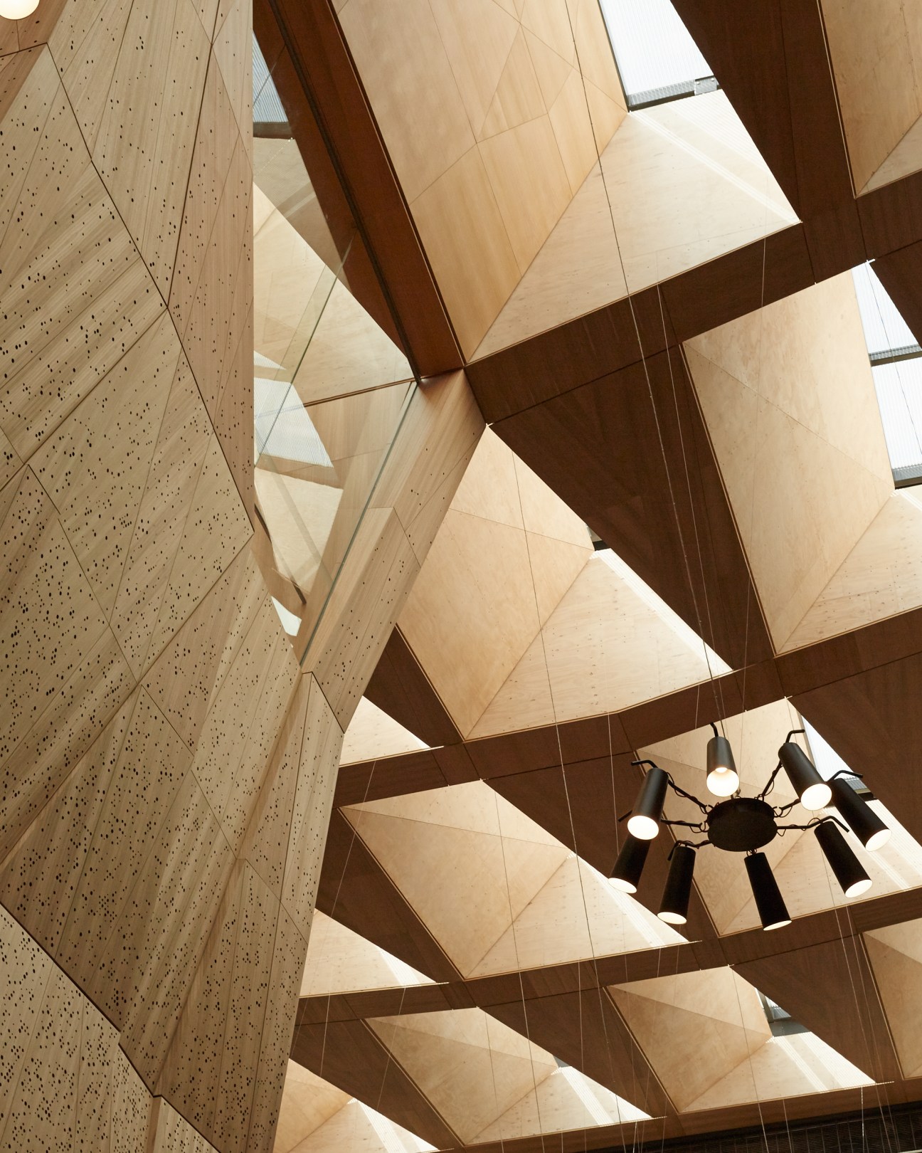 Suspended timber coffering with geometric panels and a dangling spider-pendant light fixture in the Melbourne School of Design atrium.