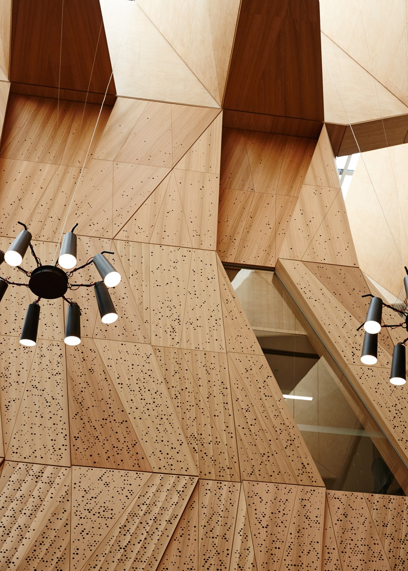 Perforated timber panels with geometric patterns and black spider-pendant lights hanging from the MSD's suspended studio ceiling.