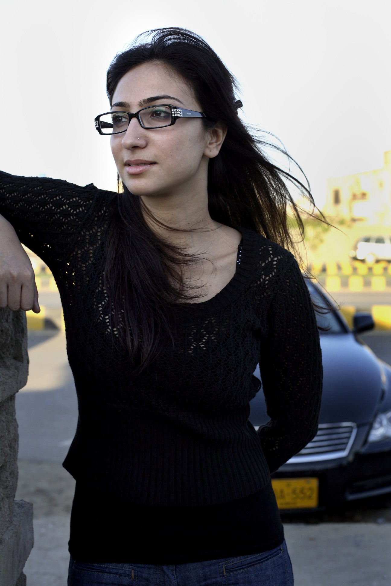 MTV Pakistan DJ Anoushey wearing glasses and a black textured top, standing outdoors with a yellow building visible in the background.