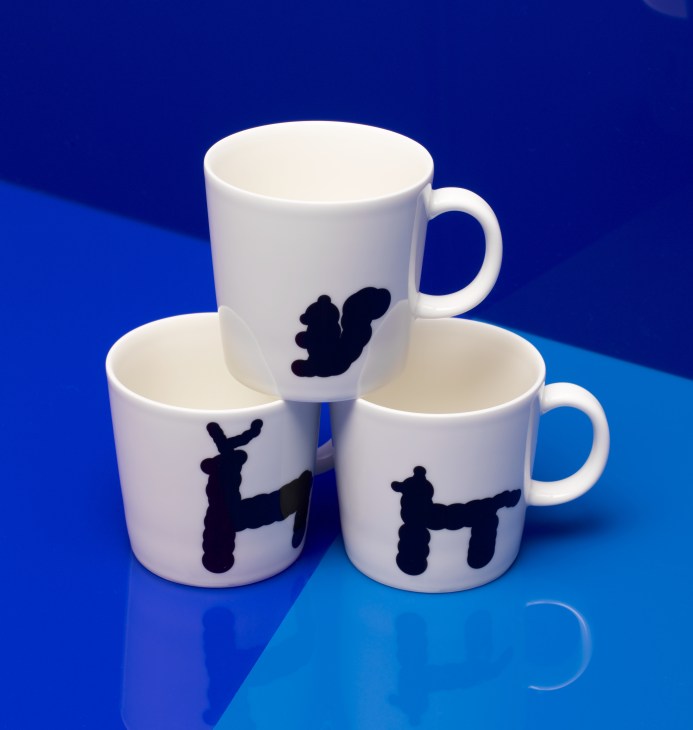 Three white ceramic mugs with black animal silhouettes on a blue background.