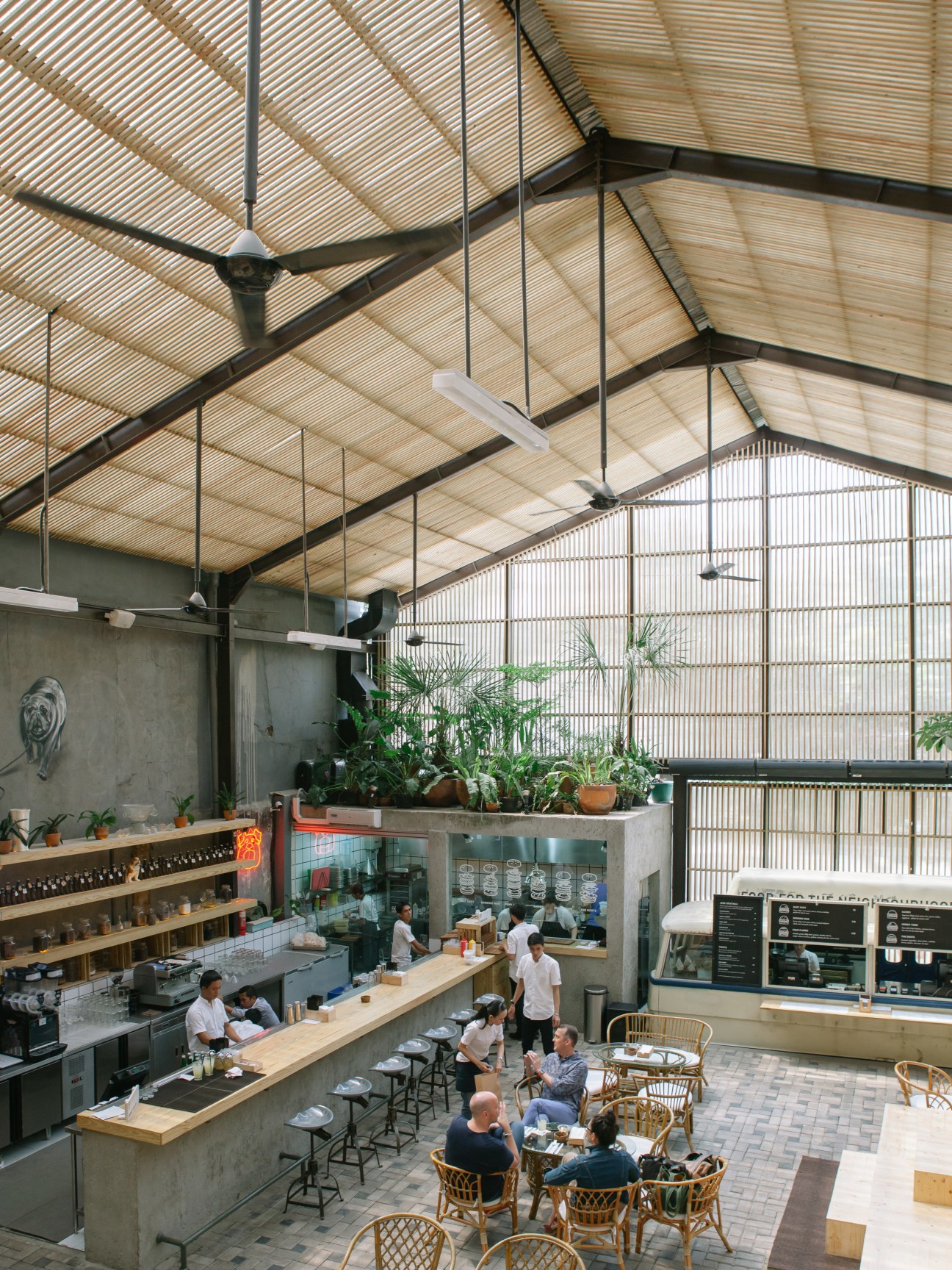 Overhead view of Three Buns restaurant in Jakarta with counter seating, plants, and industrial ceiling design.