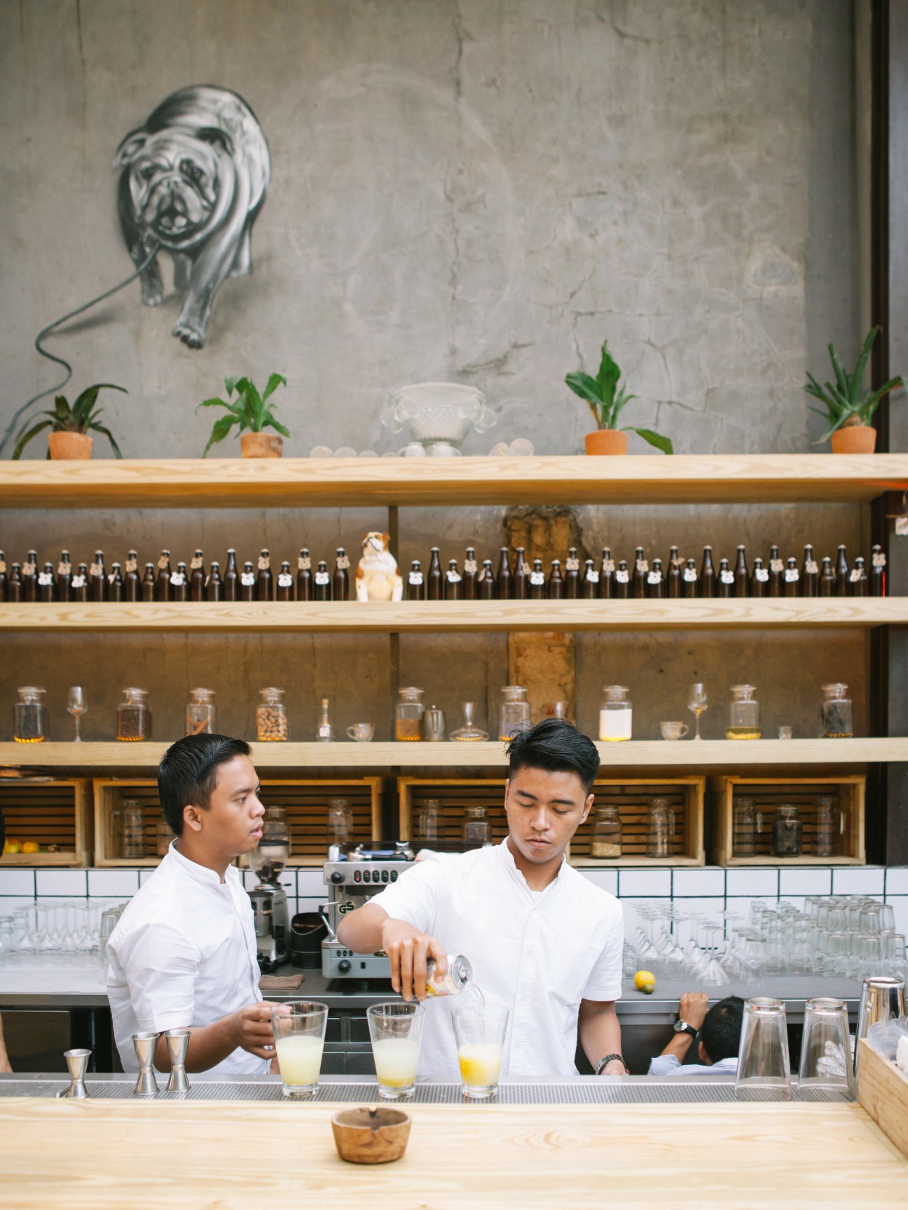 Two bartenders in white shirts prepare a cocktail at Three Buns restaurant in Jakarta.