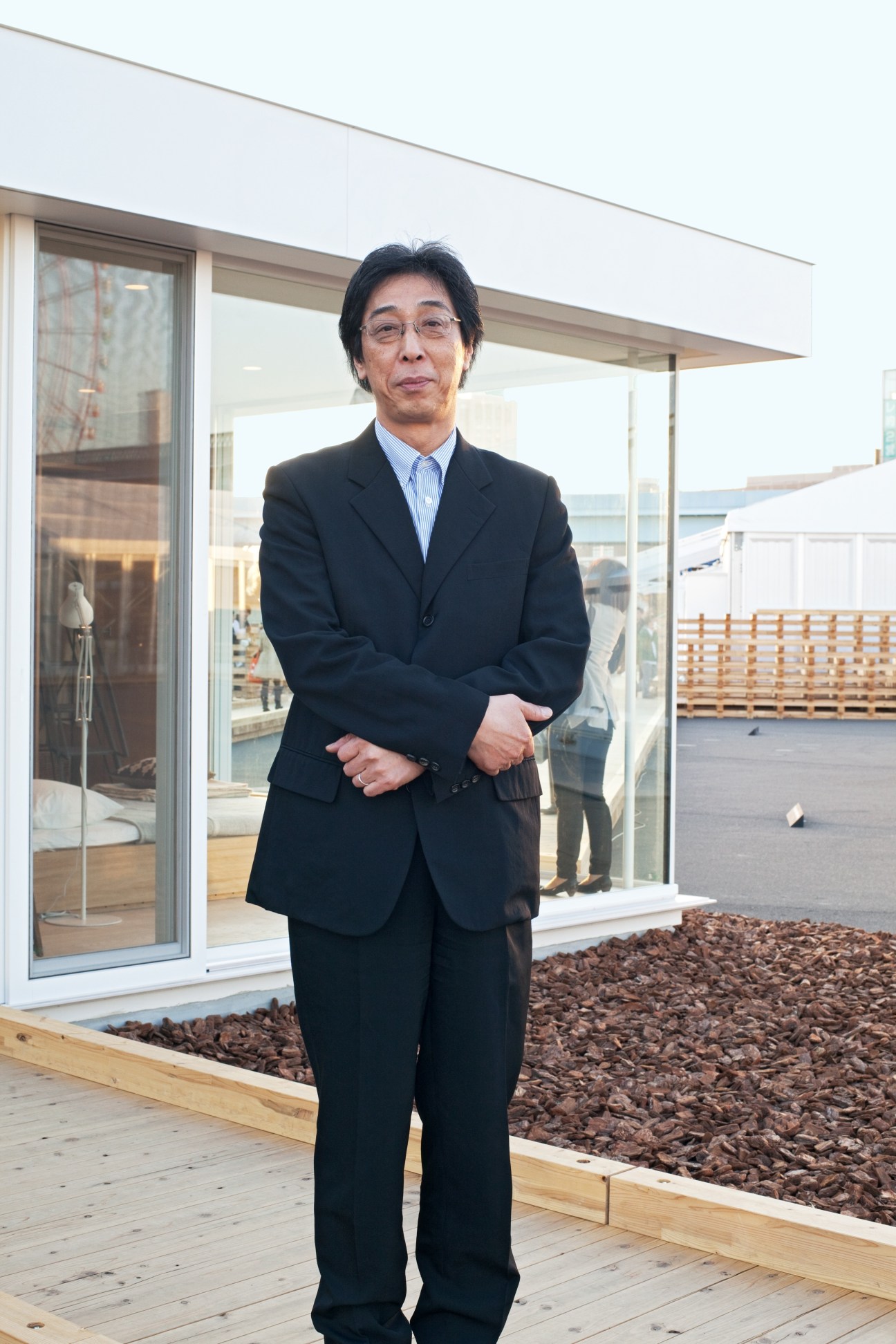 Masaaki Kanai, president of Ryohin Keikaku (Muji), standing on a modern rooftop with wooden decking and gravel landscaping.