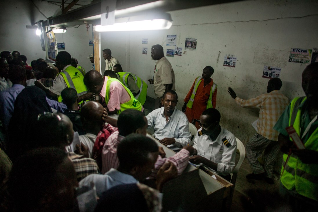 Crowded airport terminal with passengers and staff in neon safety vests during check-in rush.