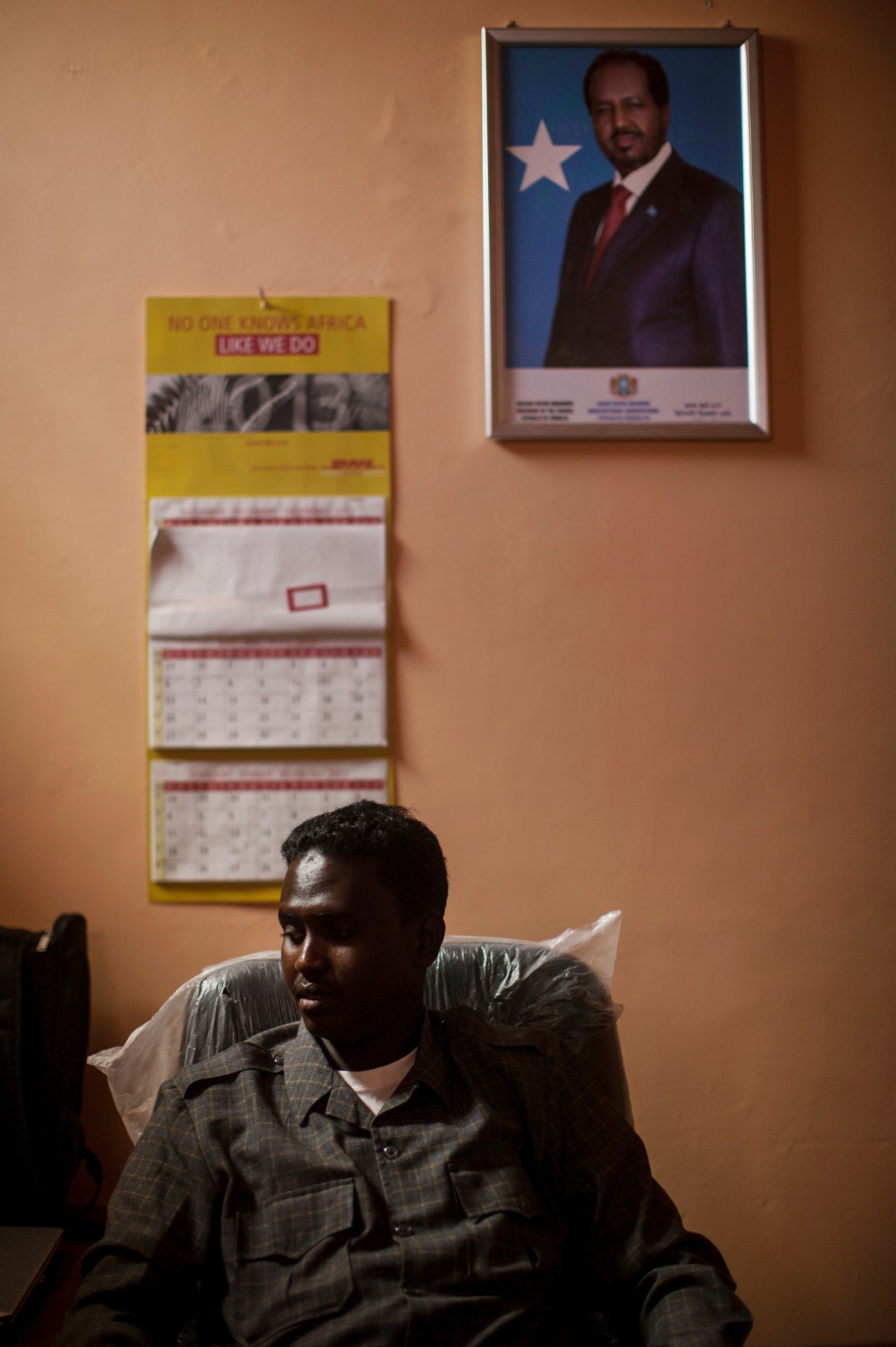 Airport manager Ahmed Ibrahim Iman sitting in an office with framed portrait and calendar on beige wall.