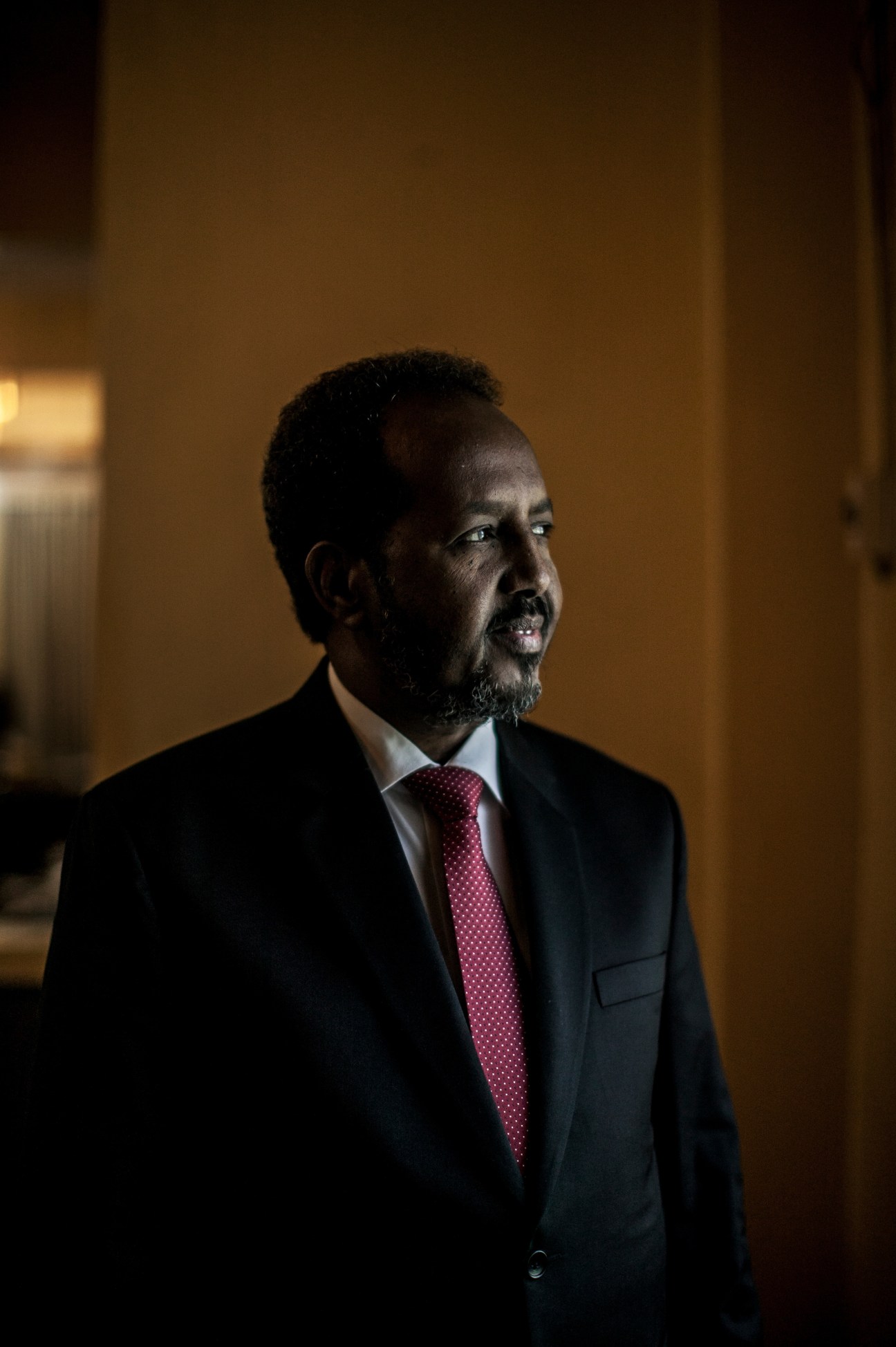 President Hassan Sheikh Mohamud in a dark suit and burgundy tie, portrait in warm lighting.