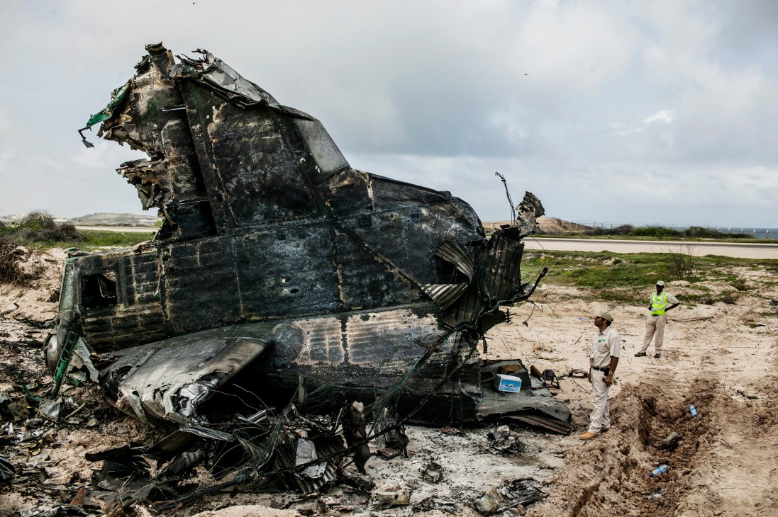 Heavily damaged Ethiopian Air Force cargo plane wreckage on barren ground with two workers examining the site.