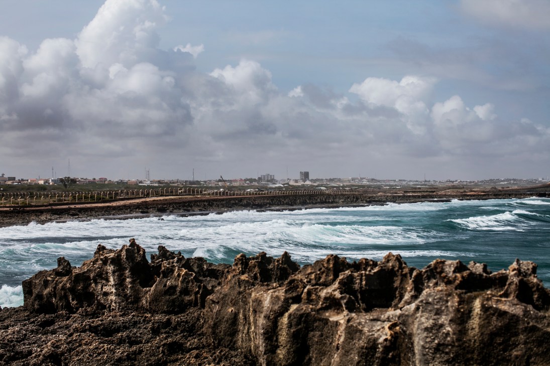 Rocky coastline with ocean waves and airport perimeter fencing stretching along Mogadishu's shore.